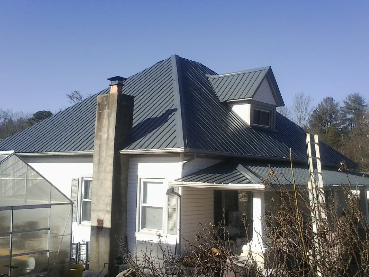 Dark blue standing seam metal roof on a white farmhouse with dormer — Slate & Tile Roof Repair by Roofing Brothers in Davis City