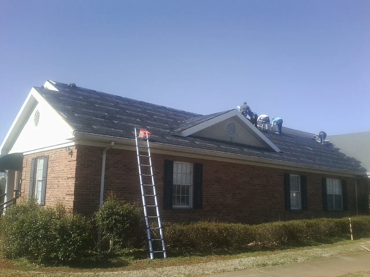 Crew tearing shingles off a brick ranch roof with a ladder set — Emergency Roof Repair work by our crew in Davis City