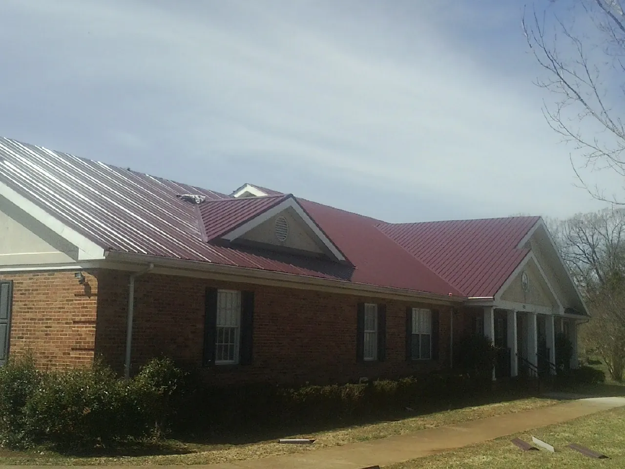 Red metal roof with gabled entries on a long brick building, from a Hail Damage Roof Repair job in Davis City