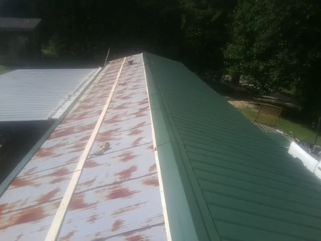 Old rusted panels beside newly installed green metal roofing — Wind Damage Roof Repair by Roofing Brothers in Davis City