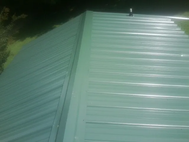 New green metal panels meeting at the ridge of a roof — Flat Roof Repair work by our crew in Davis City