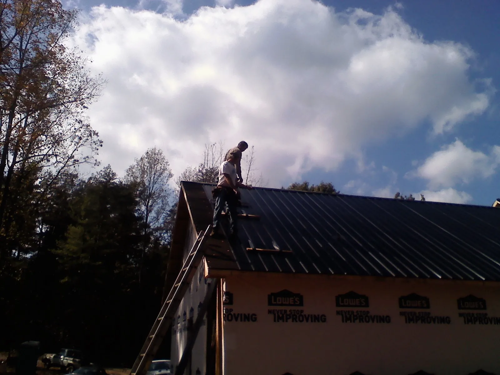 Roofer fastening dark metal panels high against a cloudy sky, from a Roof Inspection job in Davis City