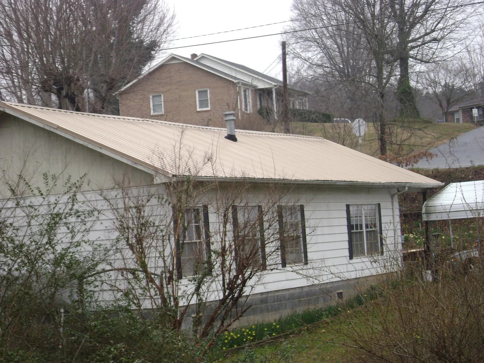 Tan metal roof on a white sided house set into a hillside — Commercial Roofing by Roofing Brothers in Davis City